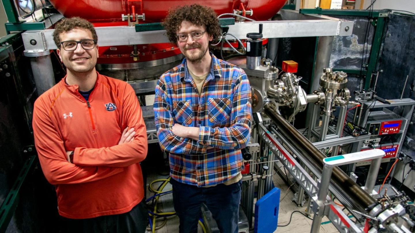 Two people stand with crossed arms in front of a large, complicated machine