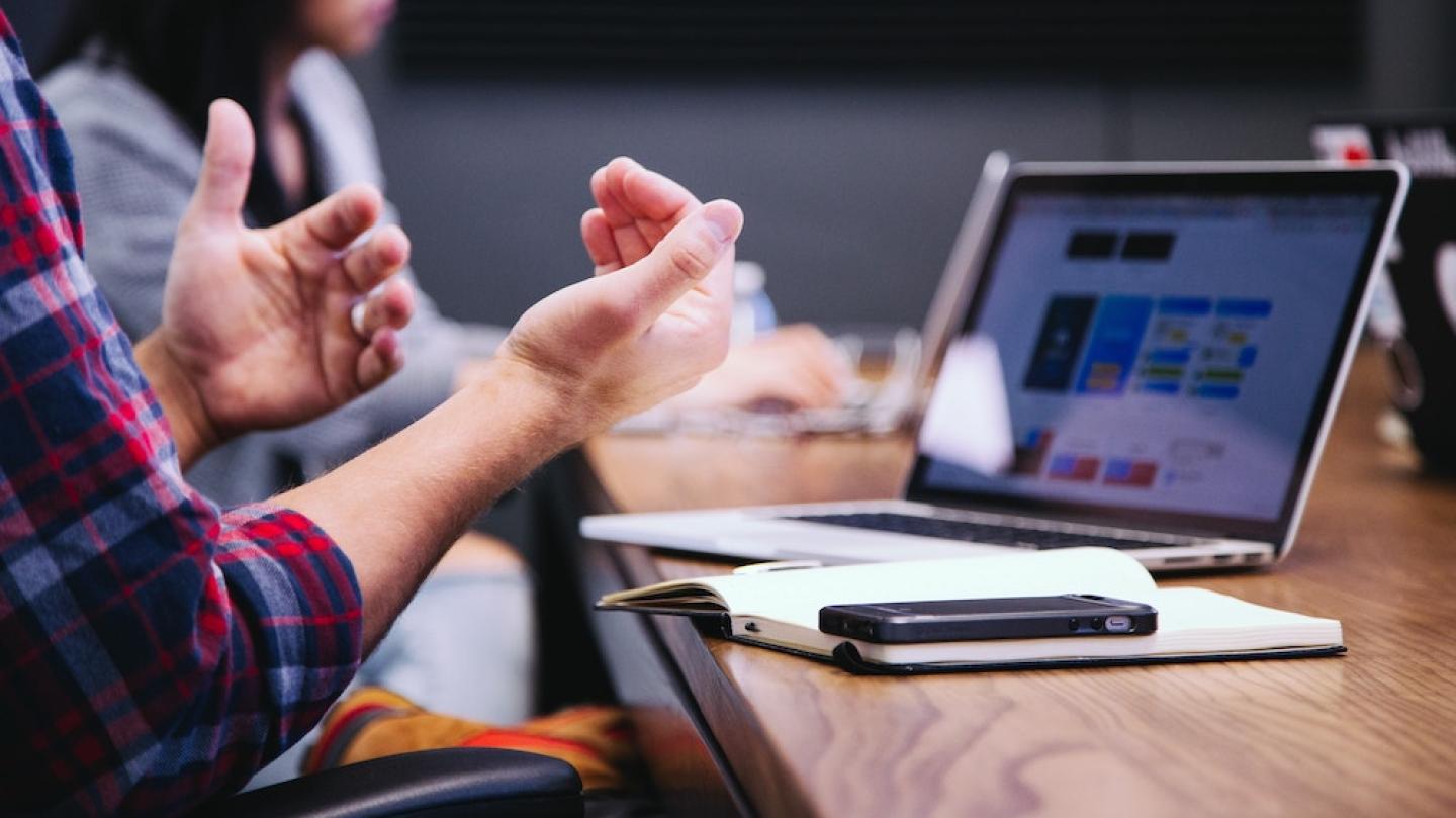 Hands gesturing in front of a laptop computer and a notebook