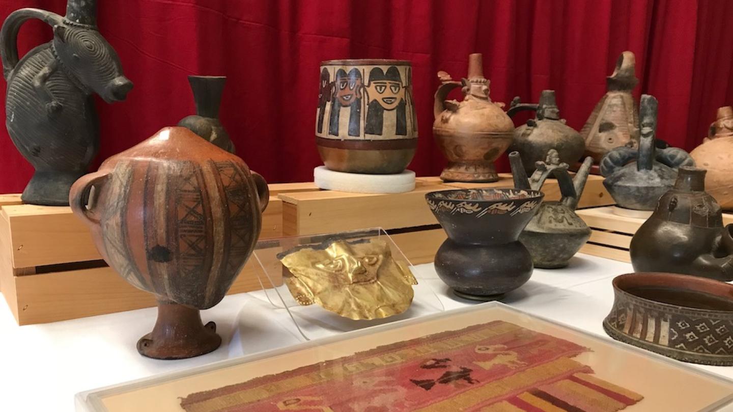 A display case showing a ceramic head-shaped object standing on a base; a woven cloth showing animal shapes; and a gold mask