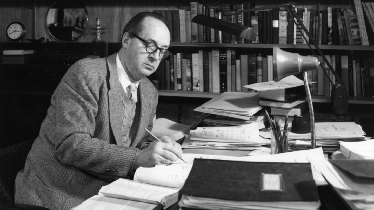 Historic black and white image: a person sitting at a desk, writing