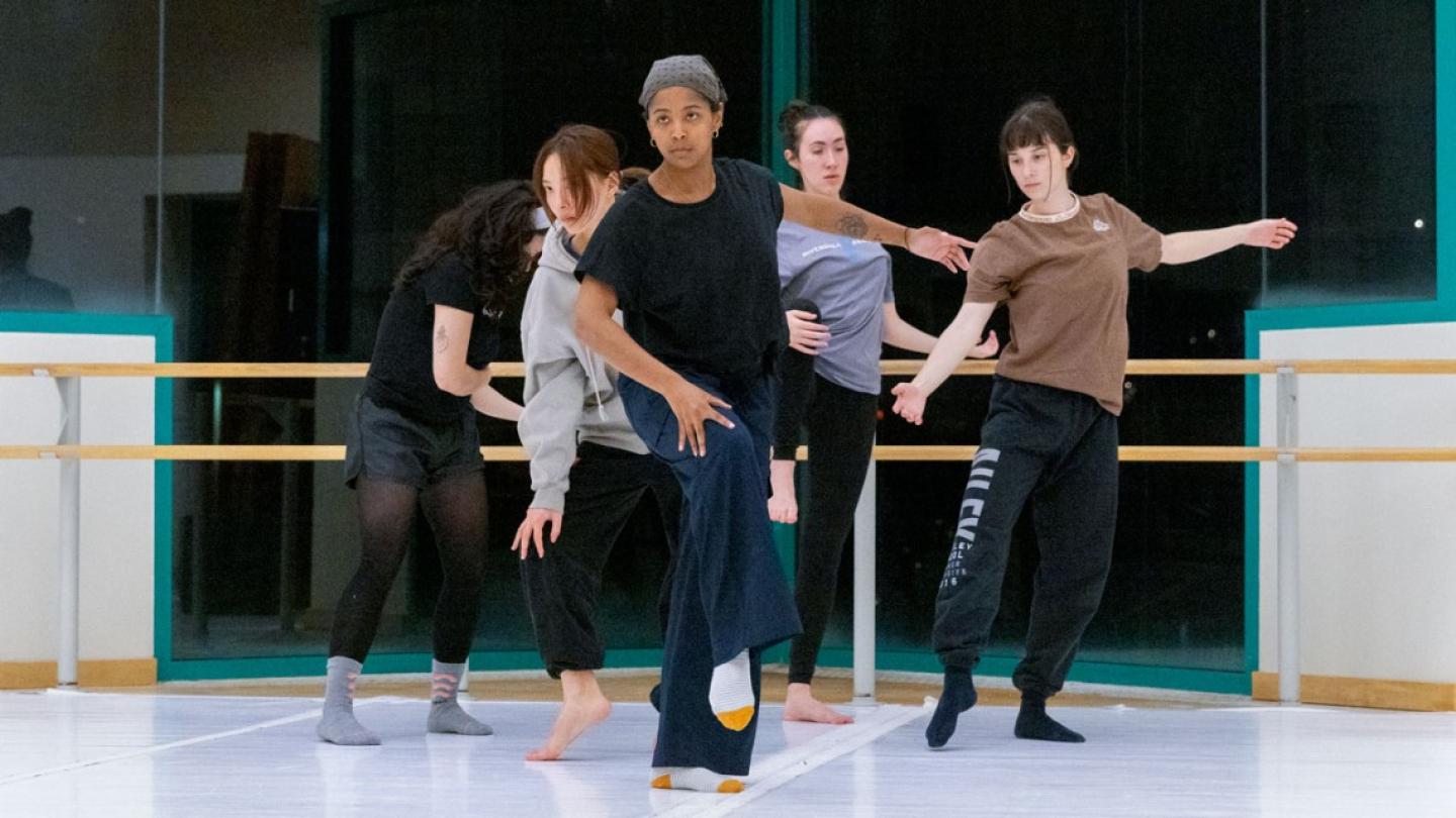 Five people perform a dance, creating a V formation with their bodies